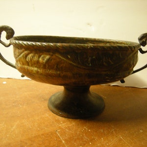 May include: A bronze bowl with two handles and a pedestal base. The bowl has a decorative design around the rim and is slightly tarnished.