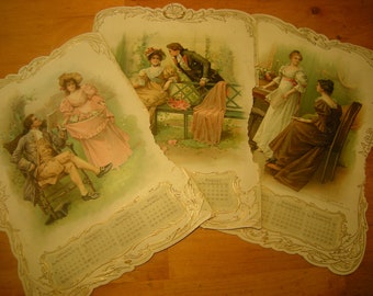 May include: Three vintage calendar cards with ornate gold borders and floral designs. Each card features a different couple in a romantic setting. The cards are for the months of April, August, and November/December.