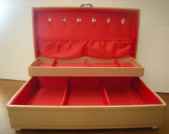 May include: A two-tiered jewelry box with a beige exterior and red velvet lining. The top tier has a row of hooks for hanging necklaces and the bottom tier has multiple compartments for storing jewelry.