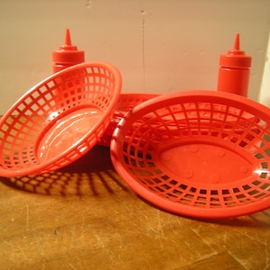 May include: Four red plastic condiment baskets with a grid pattern. Two of the baskets are oval shaped and two are round. The baskets are stacked on top of each other.