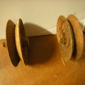May include: Two rusty metal pulleys with a screw on one side. The pulleys are stacked on top of each other.