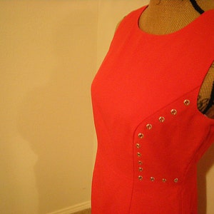 May include: A sleeveless, bright red dress with silver studs on the side. The dress is made of a smooth fabric and has a simple, classic design.