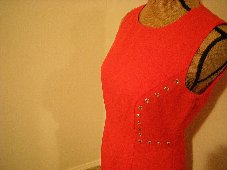 May include: A sleeveless, bright red dress with silver studs on the side. The dress is made of a smooth fabric and has a simple, classic design.