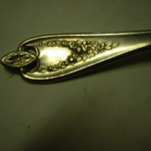 May include: Close-up of a silver spoon with ornate floral and leaf detailing. The spoon's handle features a decorative oval shape with a floral design, and the bowl has a cluster of embossed flowers.