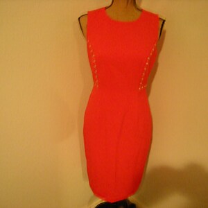 May include: A sleeveless, bright pink dress with gold accents along the sides. The dress is fitted and has a simple, elegant design.