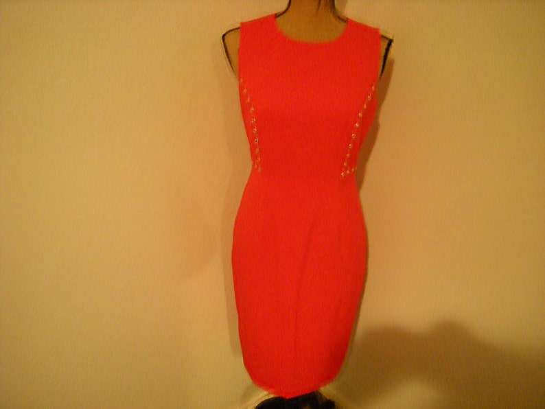 May include: A sleeveless, bright pink dress with gold accents along the sides. The dress is fitted and has a simple, elegant design.