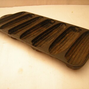 May include: A cast iron cornbread pan with six individual molds. The pan is dark gray and has a textured surface.