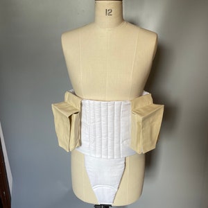 Puede incluir: Una prenda acolchada blanca con dos bolsillos beige a los lados. La prenda se muestra en un maniquí.