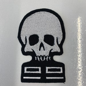 Puede incluir: Parche de hierro bordado en blanco y negro con una calavera que lleva una chaqueta con dos bolsillos.