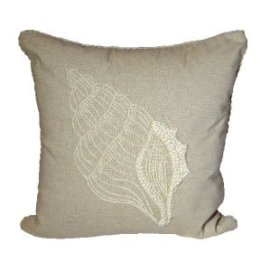 May include: A beige linen pillow with a white embroidered seashell design.
