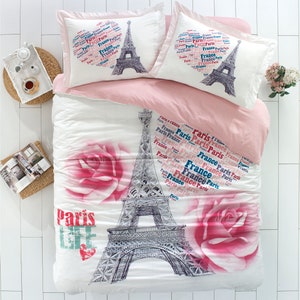 Puede incluir: Juego de cama blanco y rosa con temática parisina. La ropa de cama presenta una ilustración en blanco y negro de la Torre Eiffel con rosas rosas y el texto "Paris Life".