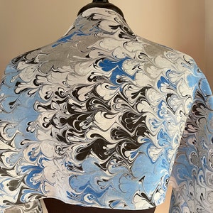 May include: A white silk scarf with a marbled pattern in shades of blue, black, and gray. The scarf is draped over a dress form.