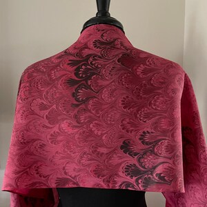 May include: A pink and black marbled silk scarf with a swirling pattern. The scarf is draped over a mannequin.