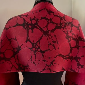 May include: A red silk scarf with a black marbled pattern. The scarf is draped over a black mannequin.