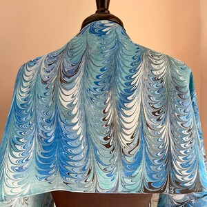 May include: A blue, white, and black marbled silk scarf with a swirling pattern. The scarf is draped over a mannequin.