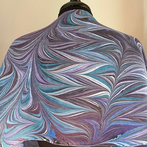 May include: A purple, blue, and white marbled silk scarf. The scarf is draped over a mannequin's shoulders.