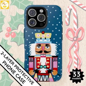 Puede incluir: Una funda de teléfono azul con un patrón de copo de nieve blanco y una ilustración colorida de un Cascanueces. La funda tiene un diseño protector de 2 capas.