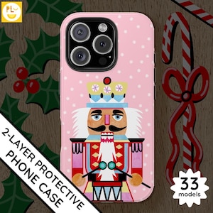 May include: Pink phone case with a white and pink nutcracker design. The nutcracker is holding a drum and has a red, white, and blue hat. The case has a polka dot pattern.