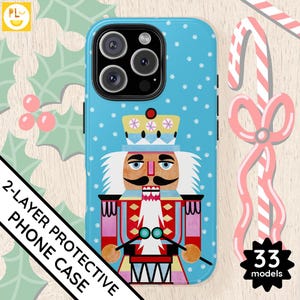 Peut inclure: Une coque de téléphone bleue avec un motif de flocon de neige blanc et une illustration de casse-noisette. Le casse-noisette porte un costume rouge et blanc et tient un tambour. La coque est étiquetée comme une coque de téléphone protectrice à 2 couches.