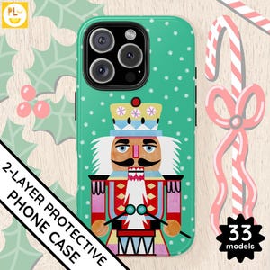 Puede incluir: Una funda de teléfono verde con una ilustración de cascanueces. El cascanueces lleva un traje rojo y blanco con una corona dorada. La funda tiene una etiqueta de "funda de teléfono protectora de 2 capas". El texto "33 modelos" está en una estrella blanca.
