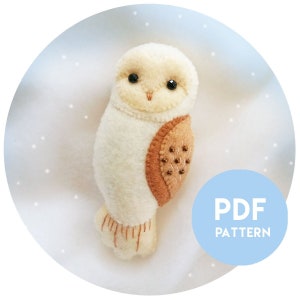 May include: A white felt owl with brown felt accents and black bead eyes. The owl is sitting on a white background with a blue circle that says "PDF PATTERN".