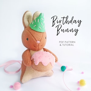 May include: A brown felt bunny wearing a green party hat with white sprinkles and holding a pink frosted cupcake. The bunny is on a white background with pink and yellow balls scattered around it. The text "Birthday Bunny" is written in black above the bunny. The text "PDF PATTERN & TUTORIAL" is written in black below the bunny.