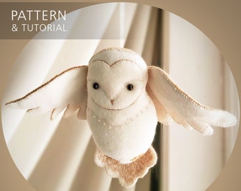 May include: A handmade white felt owl with outstretched wings, featuring black bead eyes and delicate stitching. The owl has a heart-shaped face and a small, smiling beak. The image includes the text "PATTERN & TUTORIAL" and the word "whimsylandia".