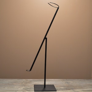 May include: A black metal display stand with a square base and a tall, angled support. The top features a curved, circular holder. The stand is designed to hold items for display.