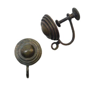 May include: Two antique bronze-toned screw-back earrings. Each earring features a circular design with concentric ridges and a central dome. One earring has a screw mechanism for attachment. The earrings are set against a white background.