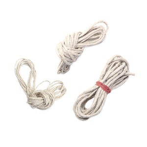 May include: Three bundles of natural-colored twine on a white background. One bundle is tied in a knot, another is loosely coiled, and the third is secured with a red rubber band. The twine appears to be made of a natural fiber.