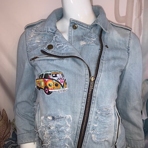 May include: Light blue denim jacket with a distressed look and a colorful embroidered patch of a vintage van with the words "Peace" and "Love Bug".