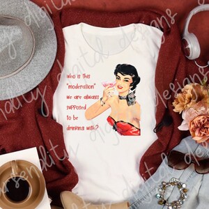 Może przedstawiać: Układ płaski z białą koszulką z ilustracją w stylu vintage kobiety z koktajlem i tekstem "who is this 'moderation' we are always supposed to be drinking with?". Zawiera szary kapelusz, słuchawki i inne akcesoria.