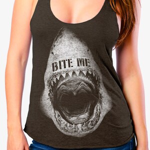 May include: Dark brown tank top with a distressed graphic of a shark's open mouth, featuring the text "BITE ME" in white. The top has a scoop neck and racerback design, suitable for casual wear.