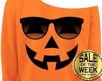 Może przedstawiać: Pomarańczowa bluza z odkrytymi ramionami z czarnym wzorem twarzy dyni, w tym okulary przeciwsłoneczne. Złota naklejka głosi "SALE OF THE WEEK ENDS SUNDAY".