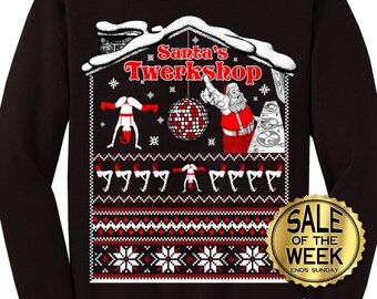 May include: Black sweatshirt with a festive design featuring Santa Claus, a disco ball, and the text "Santa's Twerkshop." The design includes pixelated snowflakes and figures in red and white. A gold "Sale of the Week" badge is also visible.