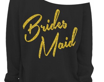 May include: Black off-the-shoulder sweatshirt with gold glitter text reading "Brides Maid". The long-sleeved sweatshirt has a relaxed fit. A small "Vintage Fly" logo is in the bottom right corner.