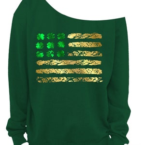 May include: A dark green off-the-shoulder sweatshirt featuring a gold and green design. The design resembles a flag with gold stripes and green shamrocks. The sweatshirt is made of a soft material and is perfect for St. Patrick's Day.