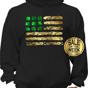 May include: Black hoodie featuring a distressed gold and green design. The design resembles the American flag, with gold stripes and green shamrocks in place of stars. A gold "Sale of the Week" sticker is visible.