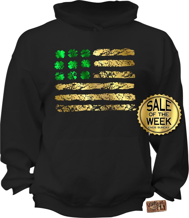 May include: Black hoodie featuring a distressed gold and green design. The design resembles the American flag, with gold stripes and green shamrocks in place of stars. A gold "Sale of the Week" sticker is visible.