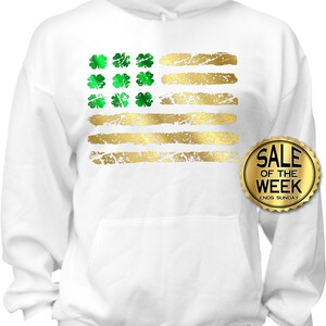 May include: White hoodie featuring a distressed gold and green design. The design resembles a flag with gold stripes and green shamrocks in the corner. The hoodie has a front pocket and a drawstring hood. The text "SALE OF THE WEEK ENDS SUNDAY" is on a gold sticker.