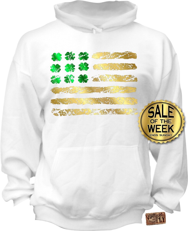 May include: White hoodie featuring a distressed gold and green design. The design resembles a flag with gold stripes and green shamrocks in the corner. The hoodie has a front pocket and a drawstring hood. The text "SALE OF THE WEEK ENDS SUNDAY" is on a gold sticker.