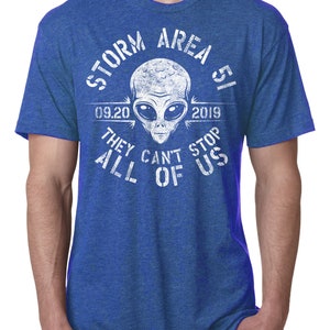May include: Blue t-shirt with a white graphic featuring an alien head and the text "STORM AREA 51 09.20.2019 THEY CAN'T STOP ALL OF US". The shirt has short sleeves and a crew neck.