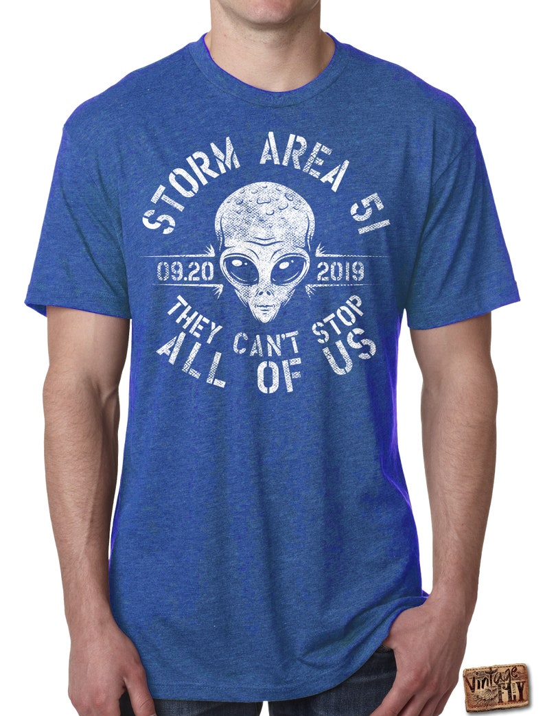 May include: Blue t-shirt with a white graphic featuring an alien head and the text "STORM AREA 51 09.20.2019 THEY CAN'T STOP ALL OF US". The shirt has short sleeves and a crew neck.