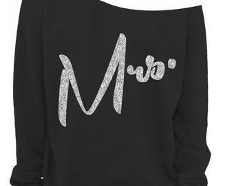 May include: Black off-the-shoulder sweatshirt with the word "Mrs." in silver glitter lettering. The sweatshirt has long sleeves and a relaxed fit. The text is in a cursive font.