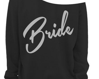 May include: Black off-the-shoulder sweatshirt with the word "Bride" in light grey script. The long-sleeved top has a relaxed fit. A small Vintage Fly logo is visible in the bottom right corner of the image.