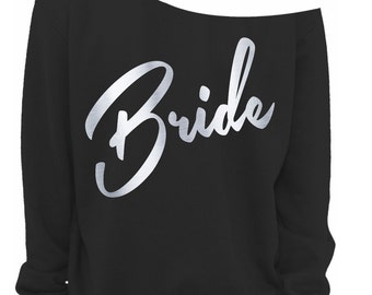 May include: Black off-the-shoulder sweatshirt with the word "Bride" in silver script across the front. The sweatshirt has long sleeves and a relaxed fit, suitable for a bridal party or hen do.