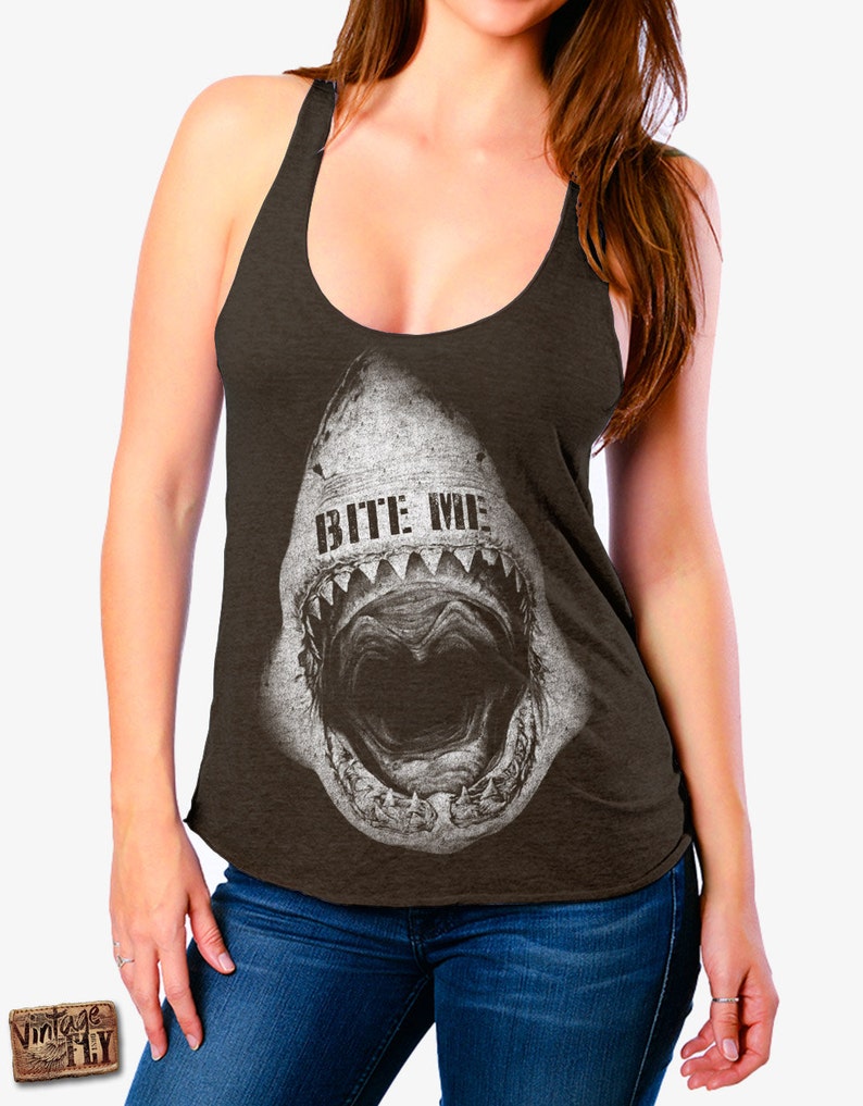 May include: Dark brown tank top with a distressed graphic of a shark's open mouth, featuring the text "BITE ME" in white. The top has a scoop neck and racerback design, suitable for casual wear.