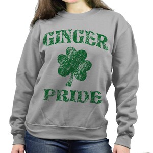 Puede incluir: Sudadera gris con las palabras "GINGER PRIDE" en letras verdes desgastadas y un tr&eacute;bol verde. La sudadera es de cuello redondo.