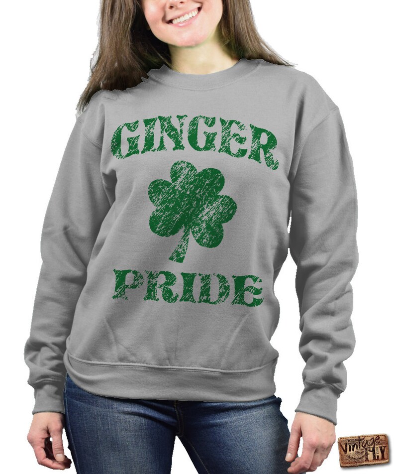 Puede incluir: Sudadera gris con las palabras "GINGER PRIDE" en letras verdes desgastadas y un tr&eacute;bol verde. La sudadera es de cuello redondo.