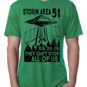 May include: Green t-shirt with a black graphic of a UFO above a forest, with the text "STORM AREA 51" and "09.20.19 THEY CAN'T STOP ALL OF US". The shirt has short sleeves and a crew neck.